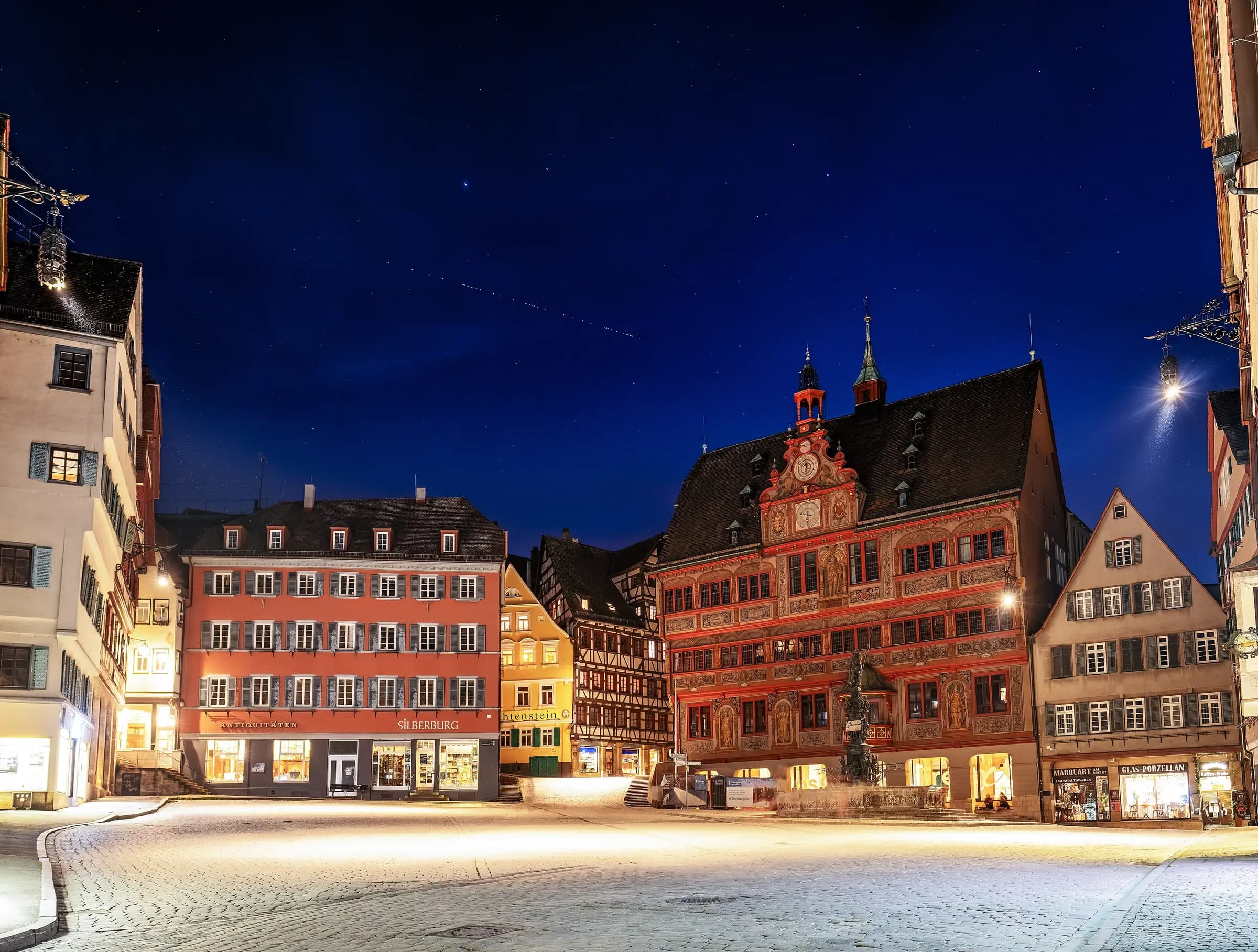 A train of satellites crossing the night sky above an old town hall and its square.