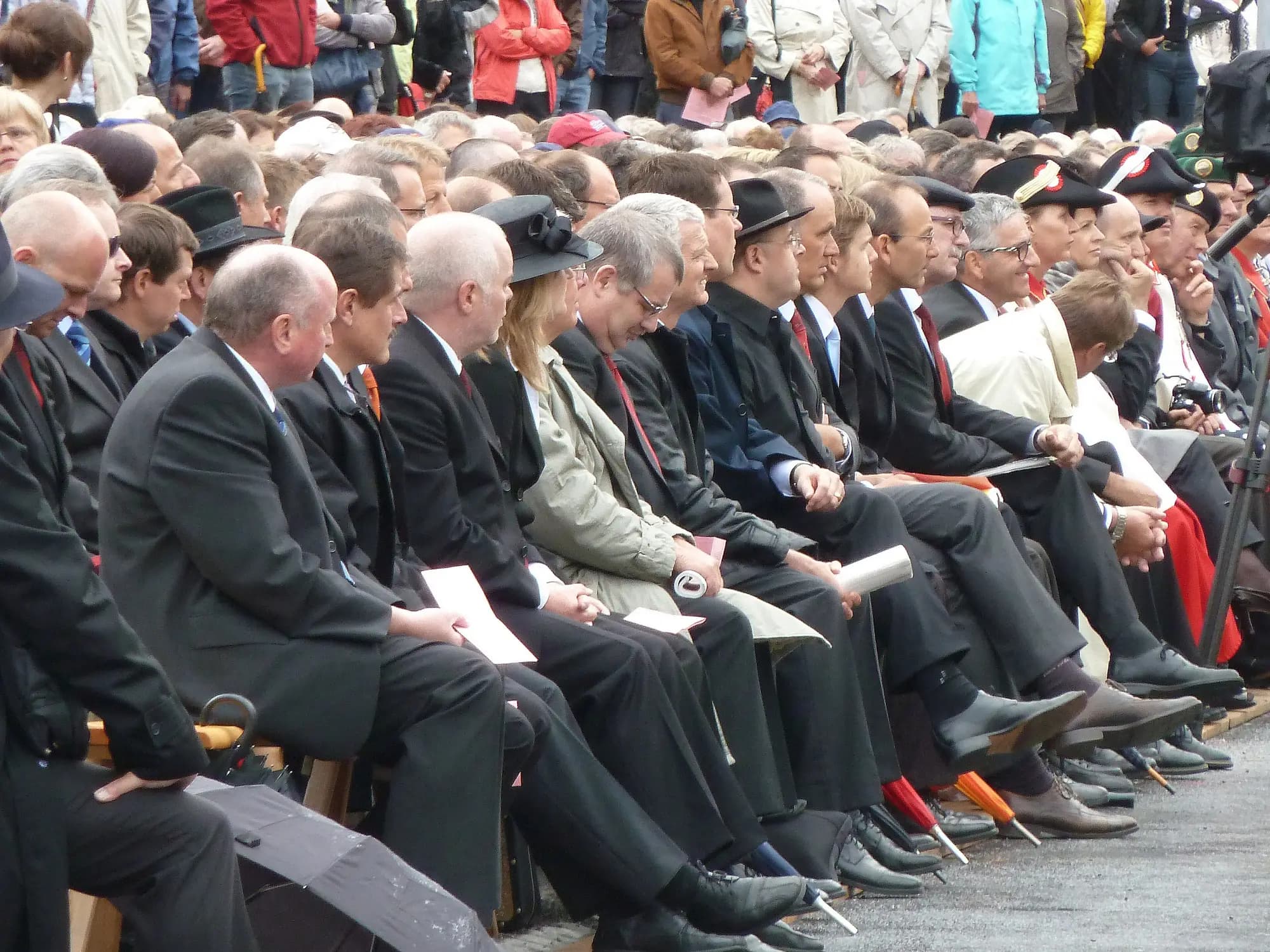 Rows of members seated side by side at an open-air assembly, papers in hand.