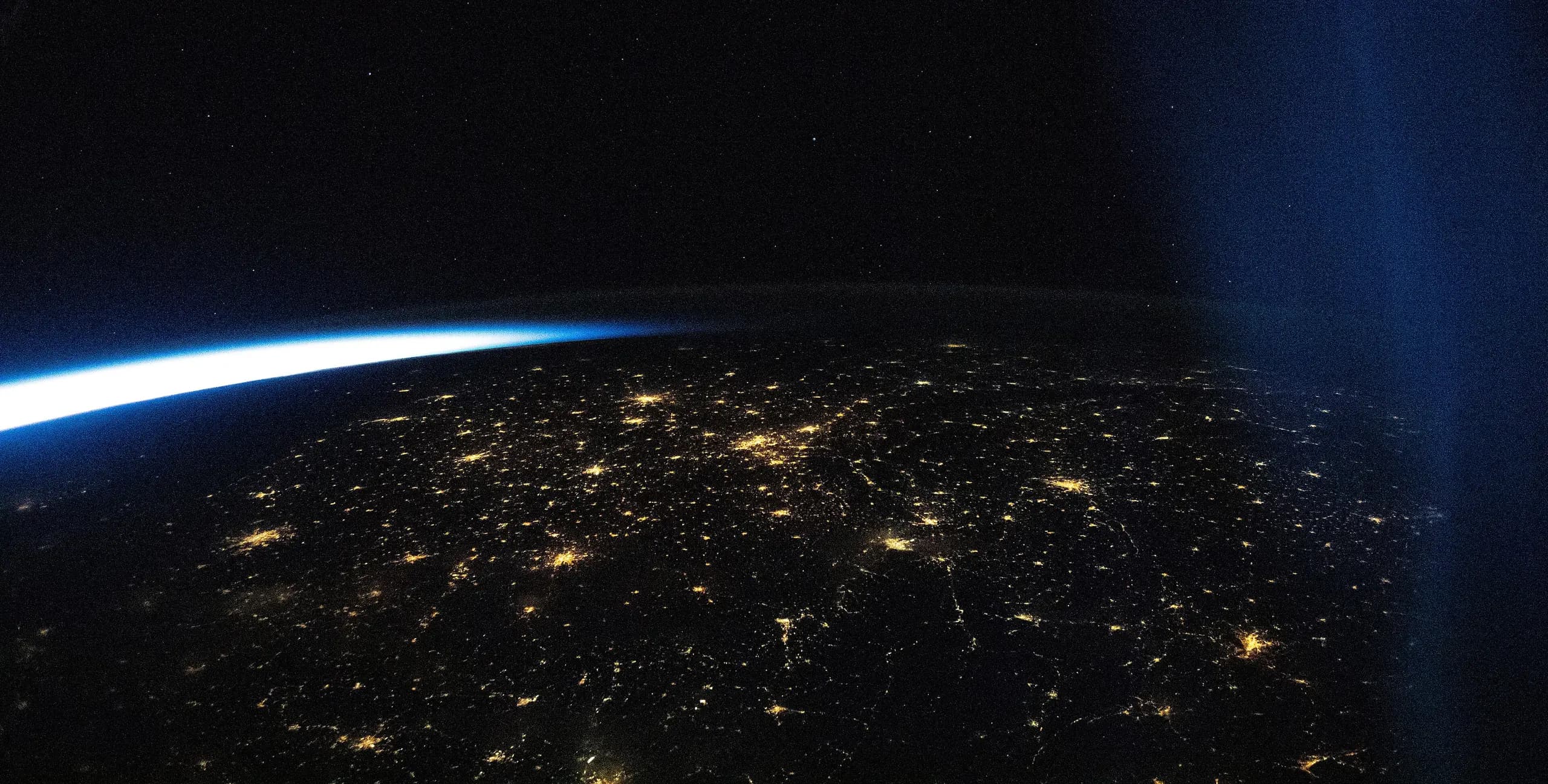 Europe's towns and cities lit up at night, seen from orbit beneath the glow of the horizon.