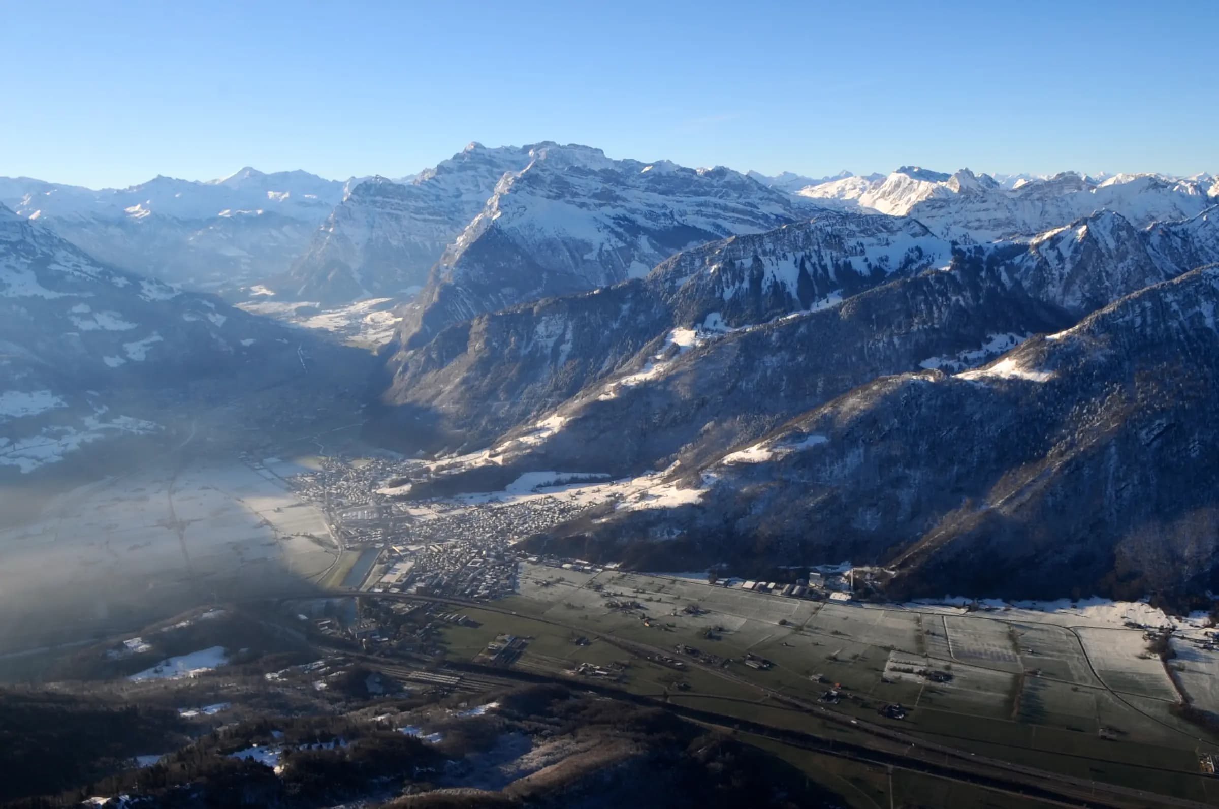 Une localité étalée au fond d'une vallée alpine aux premières lueurs, entourée de montagnes.