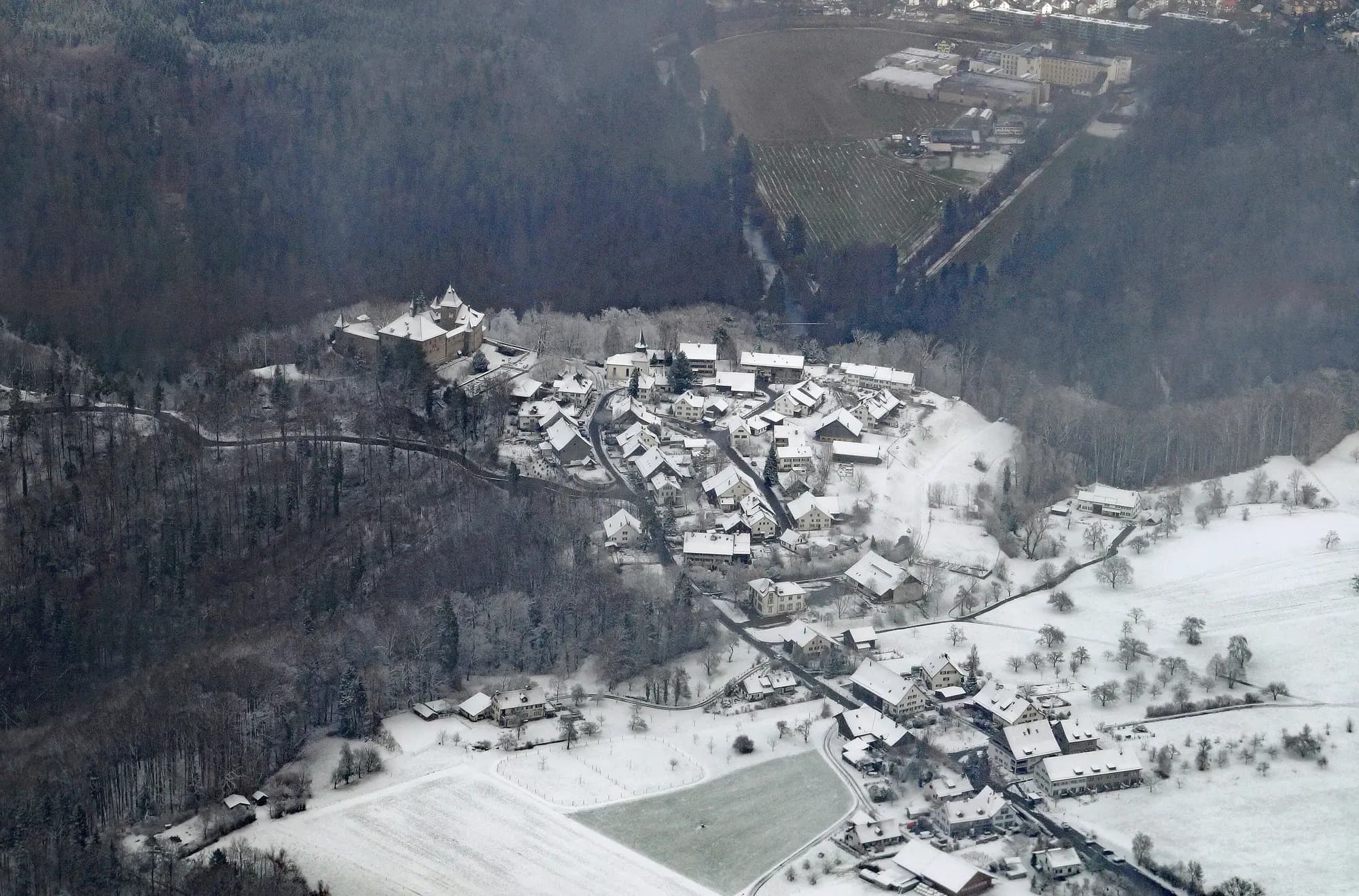 A small village and its castle on a snowy hillside, seen from the air.